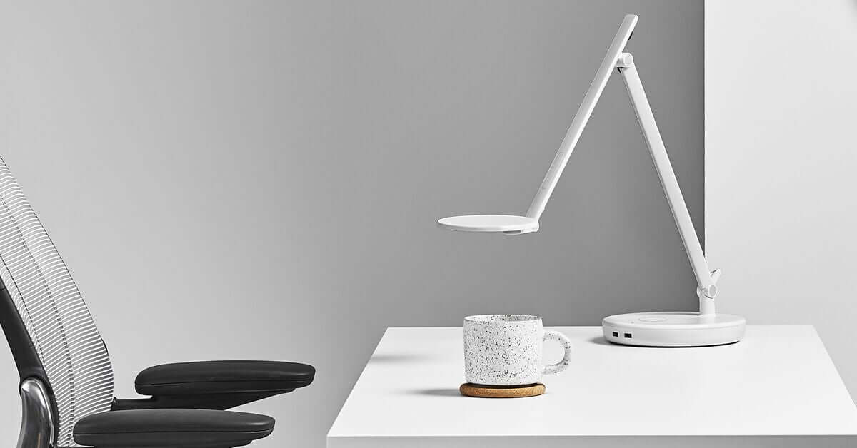 White Nova desk lamp on desktop base next to mug, showcasing modern and adaptable task lighting for workspaces.