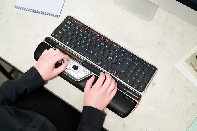 Person using RollerMouse Red with keyboard, featuring vegan leather wrist rest and ergonomic roller bar on a desk.