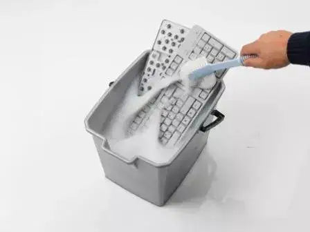 Easyclean keyboard being washed with soap, showcasing removable keys for effortless cleaning in a gray basin.