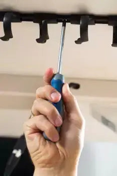 Hand installing RIB cable tray under tabletop using a screwdriver for organizing cables.