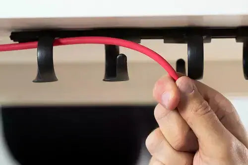 Hand organizing cables with RIB cable tray under desk for tidy workspace management.