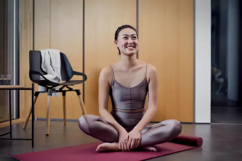 Woman in workout gear sitting cross-legged on a yoga mat next to a Numo active chair.