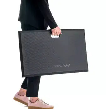 Person carrying ergonomic workstation mat for standing desks, promoting comfort and energy efficiency.