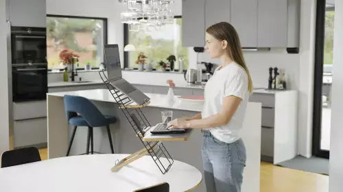 Woman using ergonomic Standfriend in light grey while working in kitchen, demonstrating versatile standing desk solution.