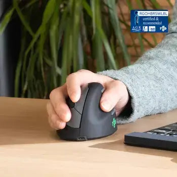 Ergonomic R-Go HE vertical mouse in use, promoting forearm movement to reduce RSI risk, shown on a desk next to a keyboard.