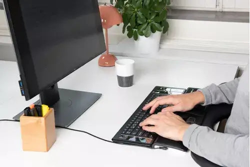 Person typing on ergonomic keyboard with solar panels next to monitor in a modern office setup.