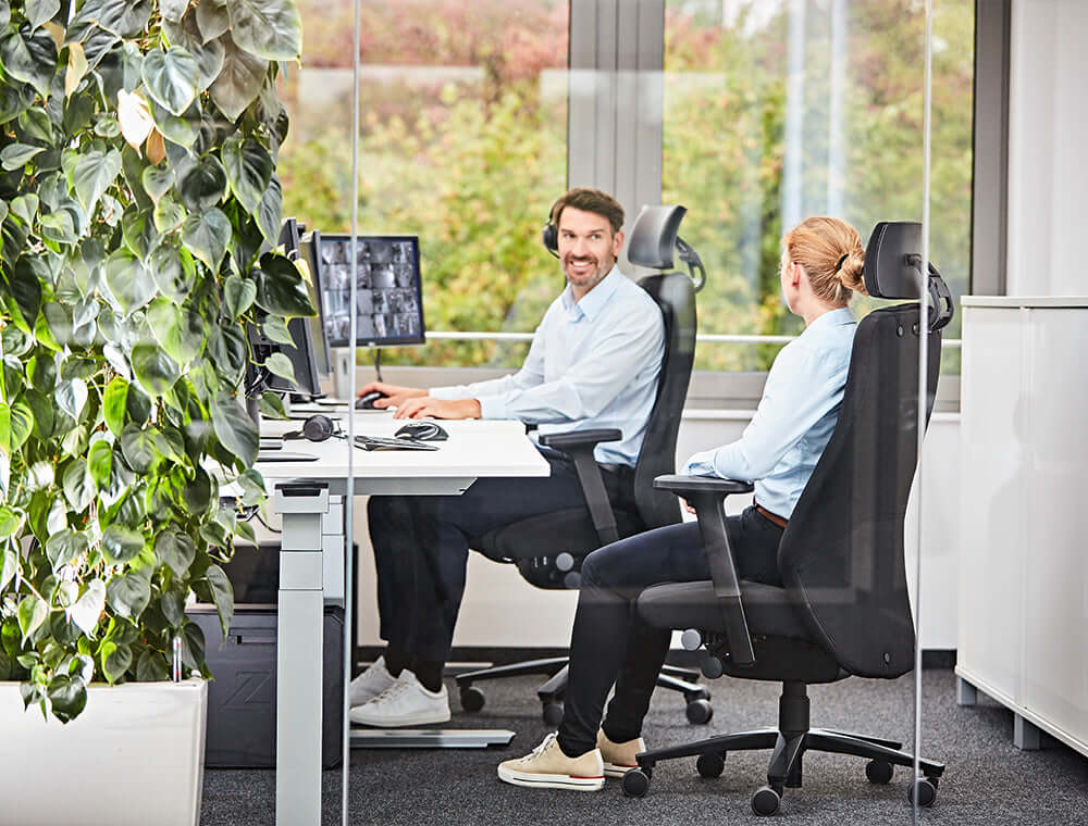 Two people sitting in TWENTYFOURis5 ergonomic chairs in a control room setting with plants and large windows.