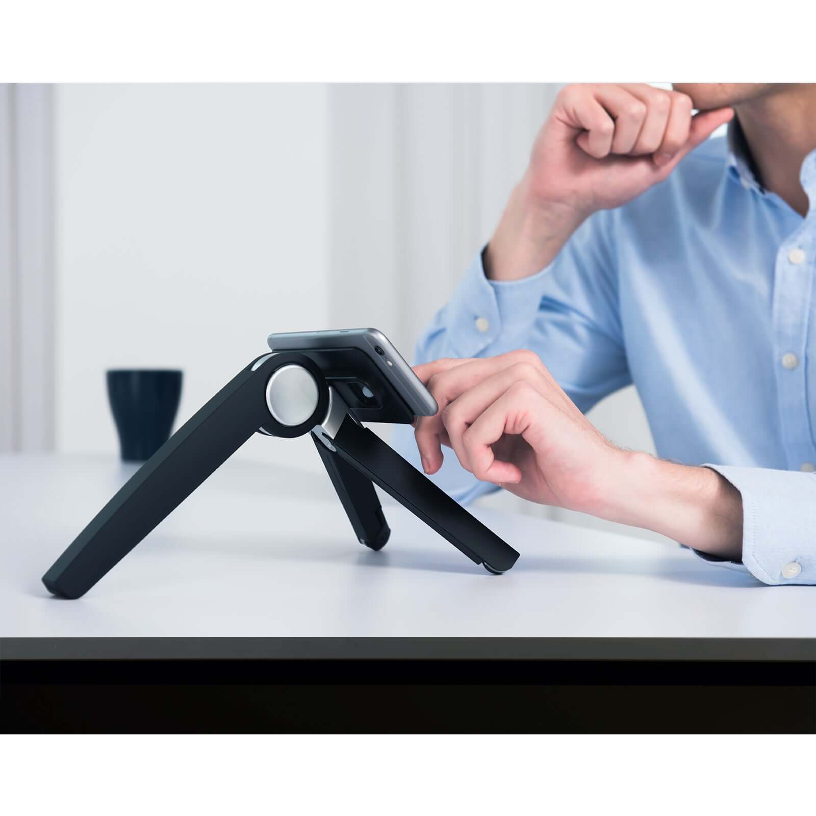 Person using black Spider laptop and tablet stand on desk for ergonomic workspace setup.