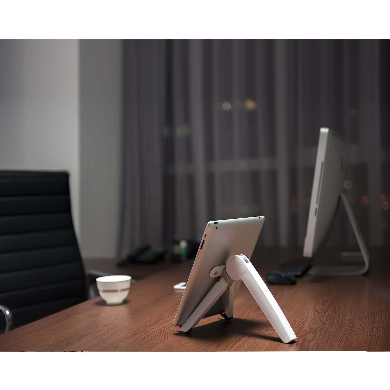 White Spider laptop and tablet stand holding a tablet on a wooden desk in a modern office setting.