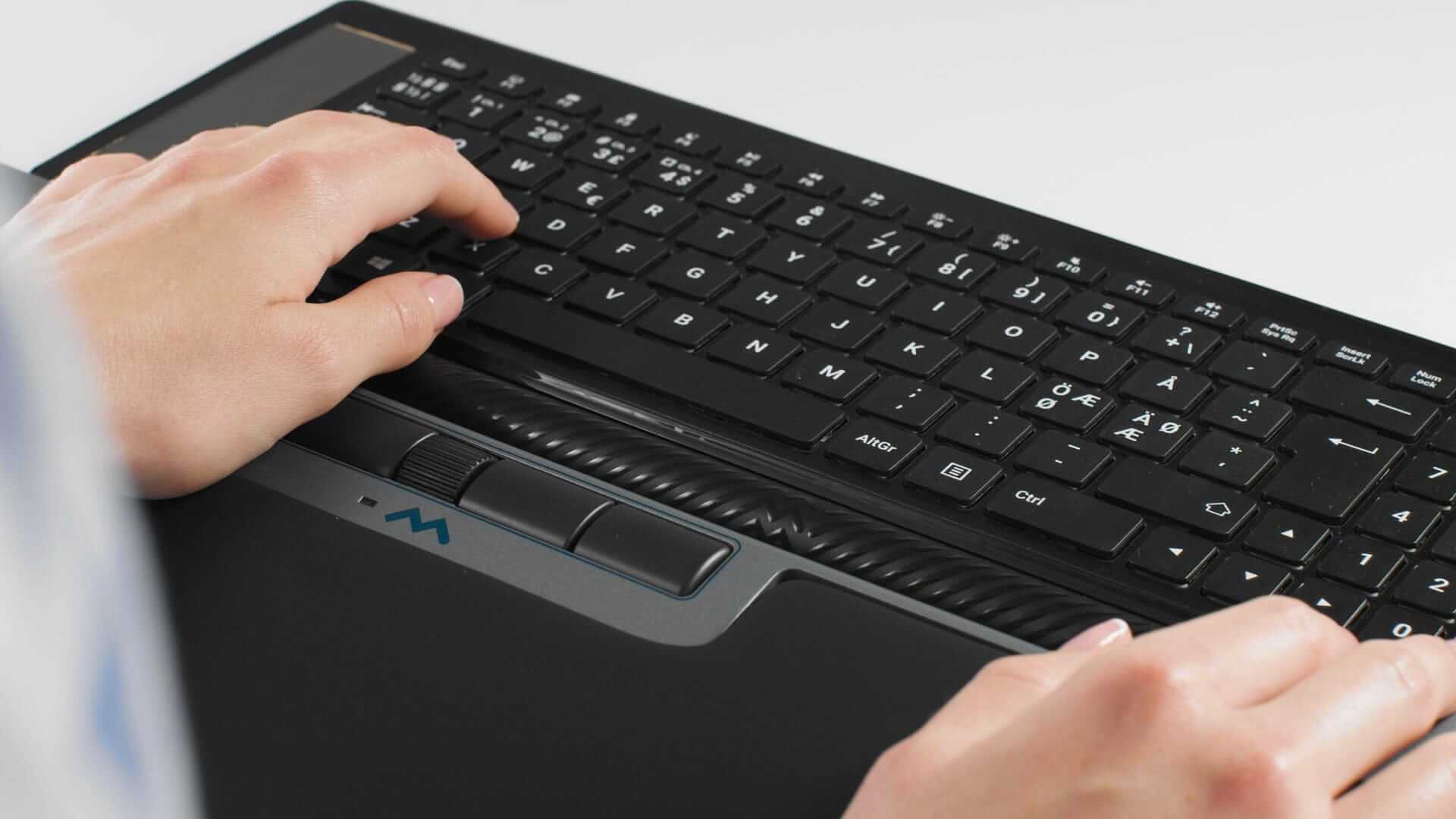 Hands typing on a black Mousetrapper Delta Extended keyboard with smooth surface and programmable buttons.