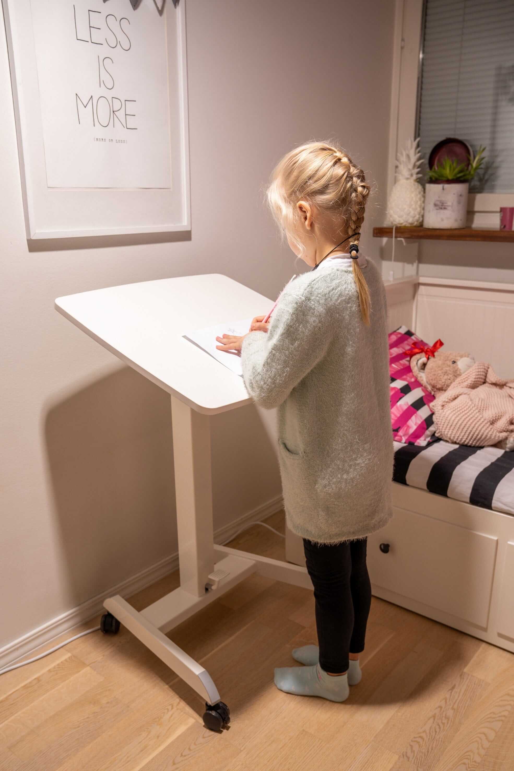 Child using GetUpDesk Tilt adjustable desk in a cozy room, featuring wheels and height adjustment for versatile use.