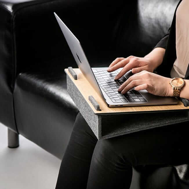 Person using a laptop on the Läpsteri laptop stand in an office setting, showcasing ergonomic design and functionality.